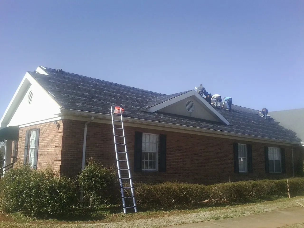 Crew tearing shingles off a brick ranch roof with a ladder set — Metal Roof Repair work by our crew in Union Point