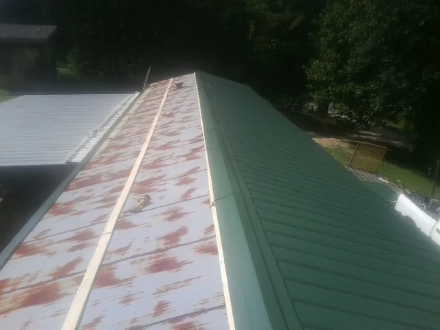 Old rusted panels beside newly installed green metal roofing — Wind Damage Roof Repair by Roofing Brothers in Union Point