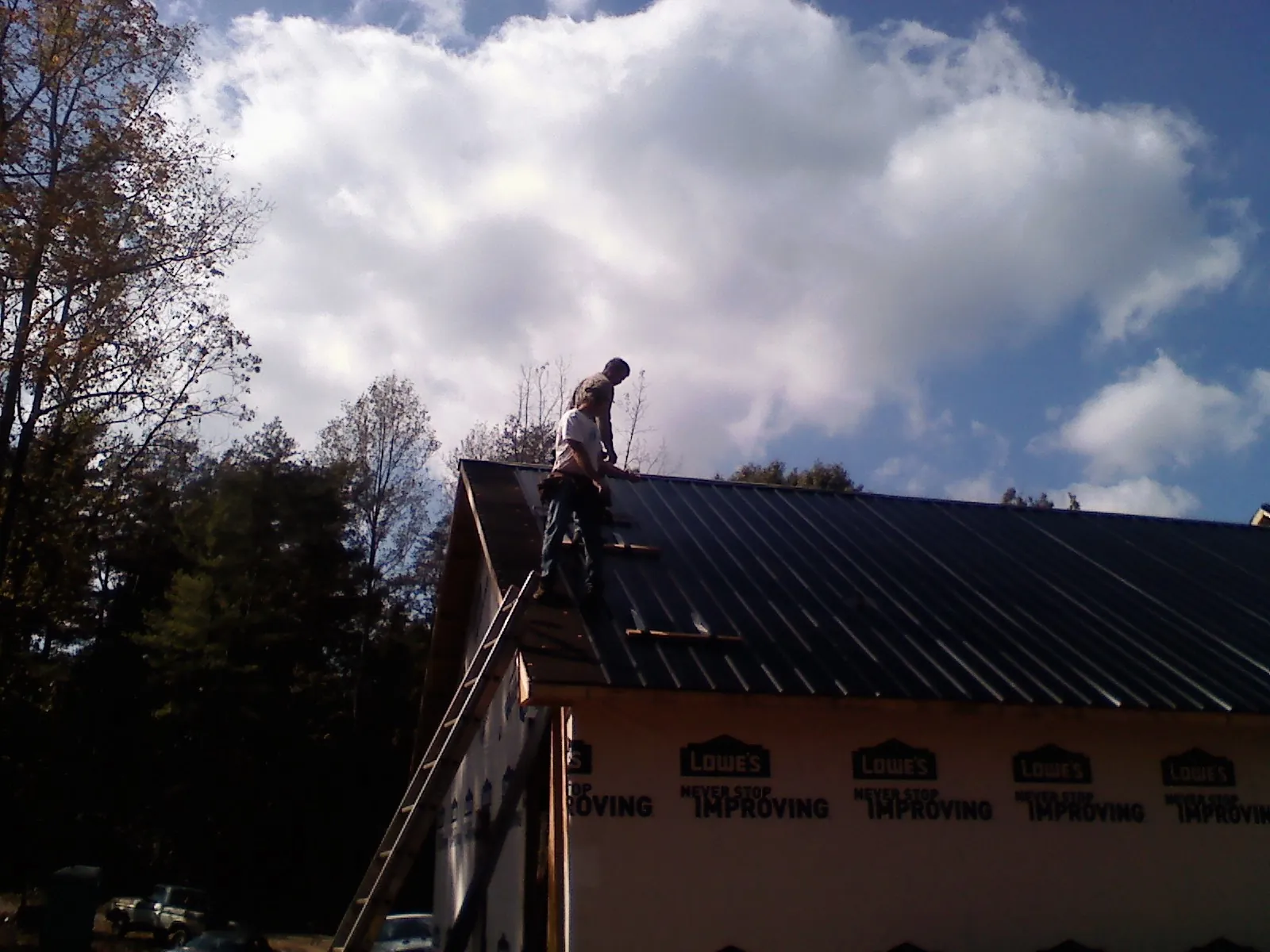 Roofer fastening dark metal panels high against a cloudy sky, from a Roof Inspection job in Union Point